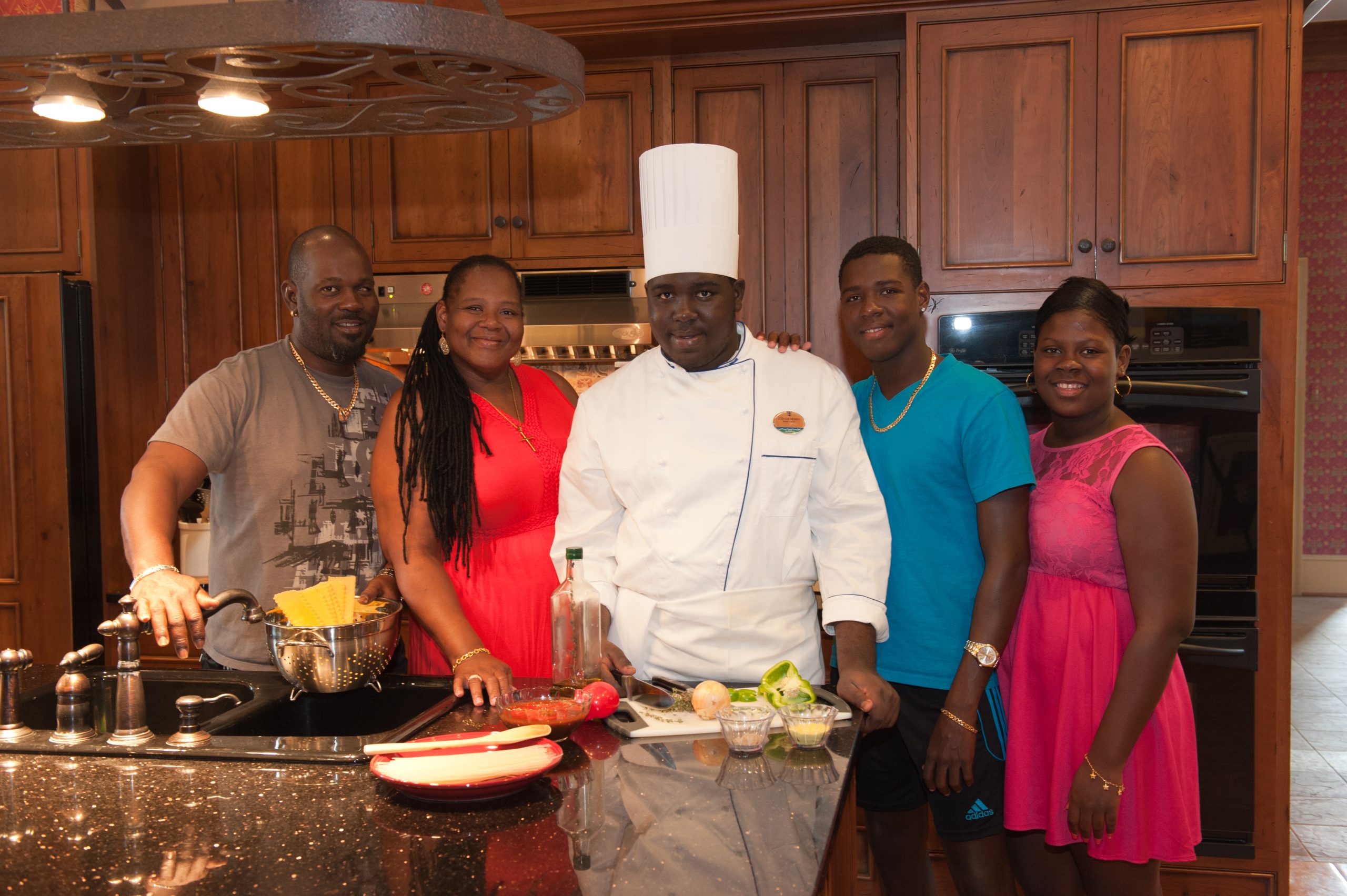 Josh Sobers-Henry, in white chef hat and clothes preparing food, and Family in The Woodmont House kitchen