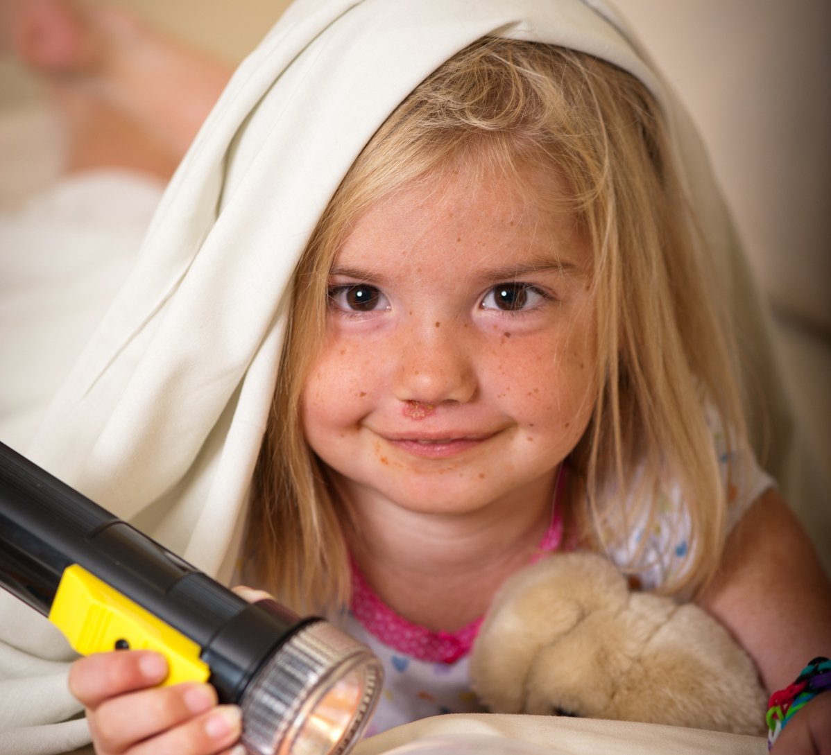 Makenna, little girl, with flashlight under blanket holding a teddy bear