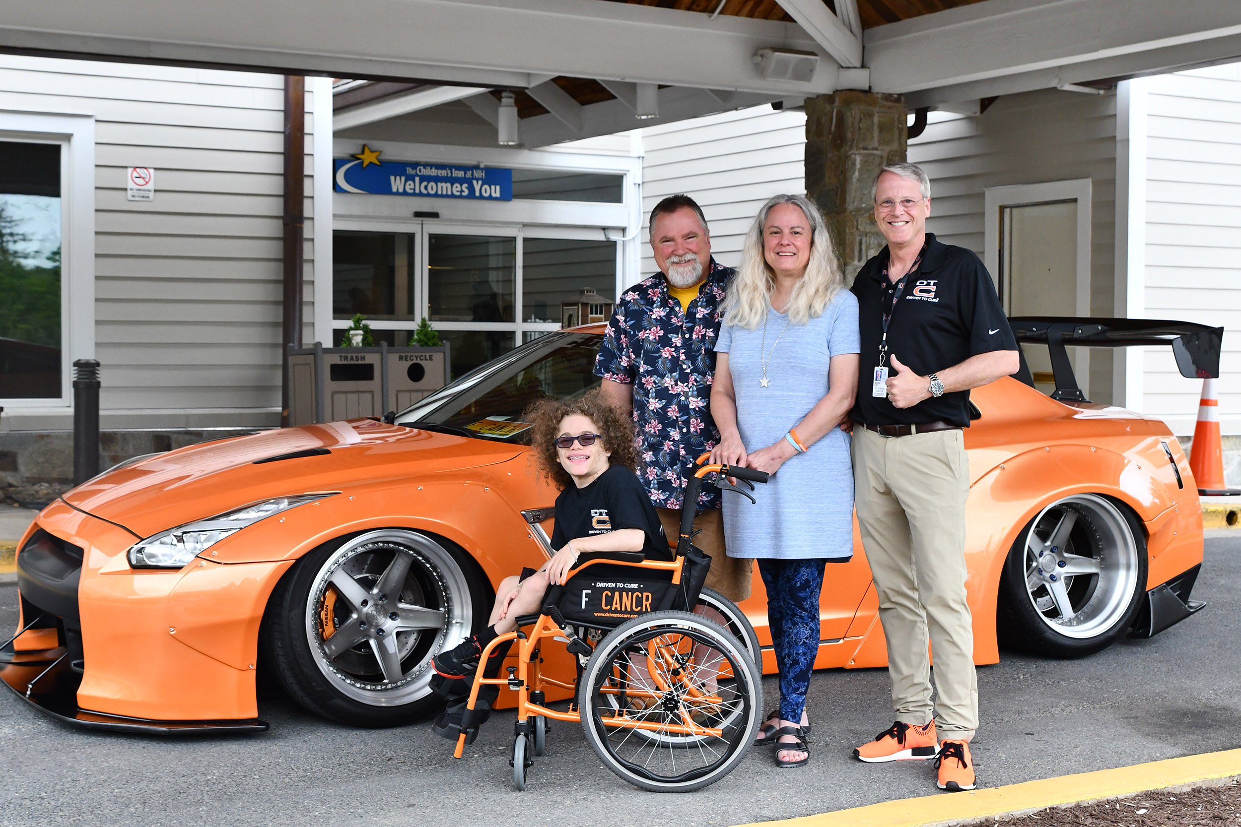 Isaac in his new wheel chair outside in front of The Inn with a DTC car